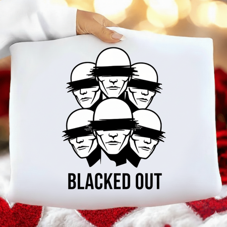 White pillow with black graphic design of faces with blindfolds and 'BLACKED OUT' text, held against a blurred background.