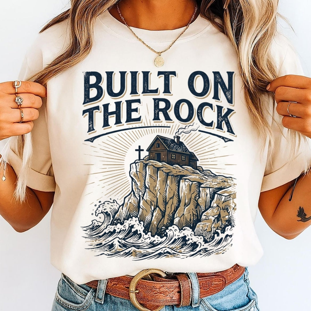 Person wearing a t-shirt with 'Built on the Rock' design and illustration of a house on a cliff.