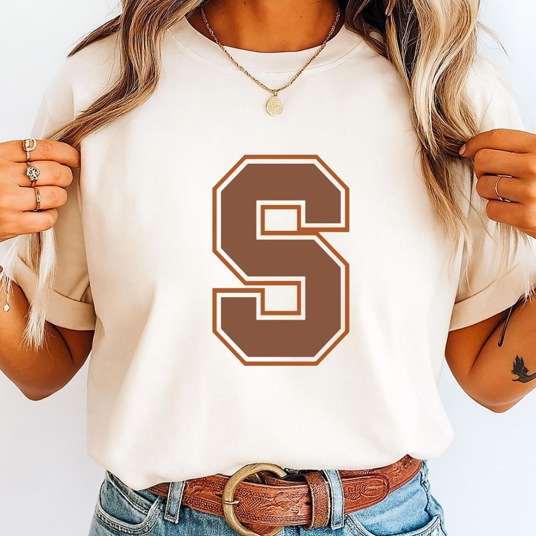 Person wearing a white t-shirt with a brown 'S' design, holding hair with a plain background.