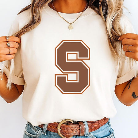 Person wearing a white t-shirt with a brown 'S' design, holding hair with a plain background.