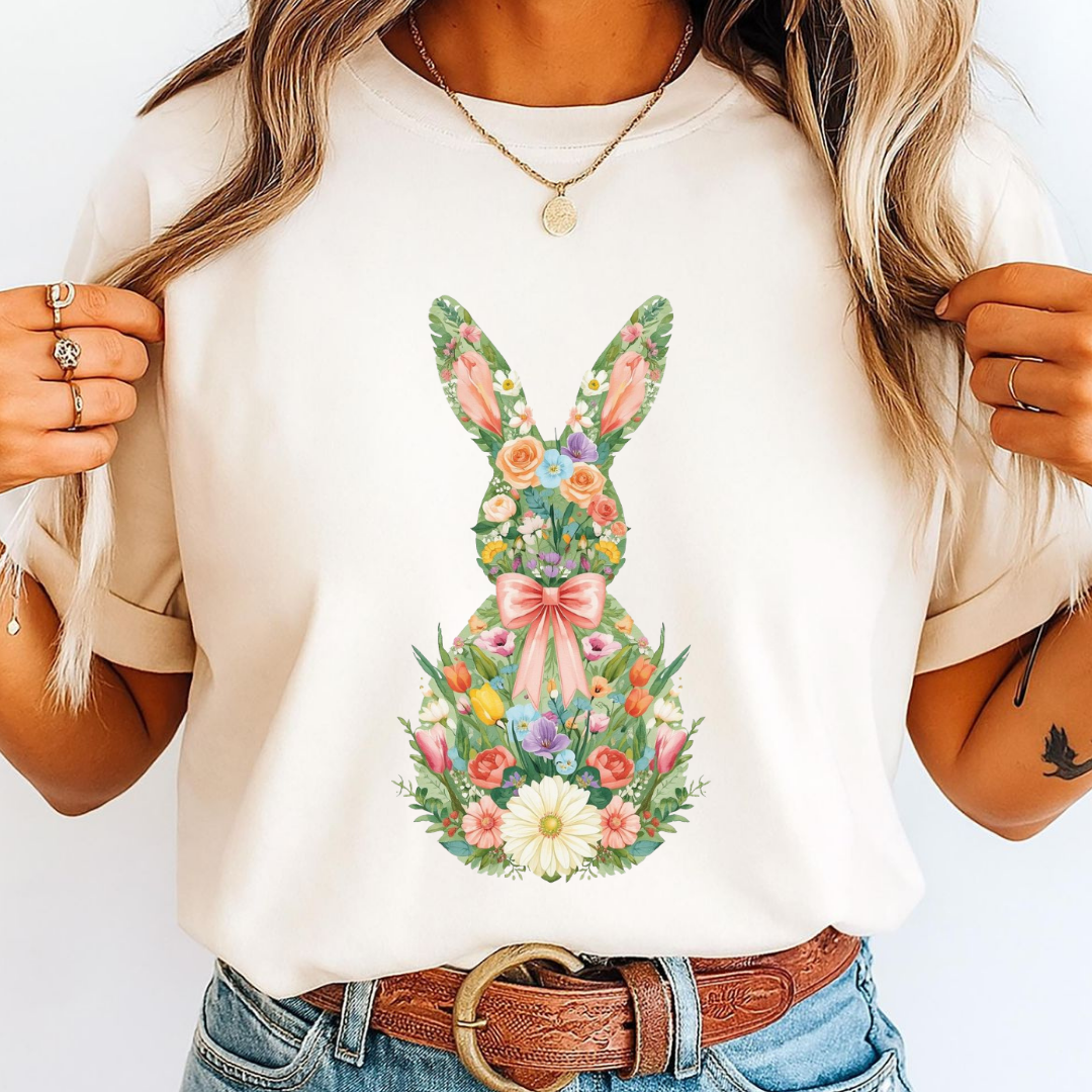Person wearing a white t-shirt with a floral bunny design, holding a white bag.