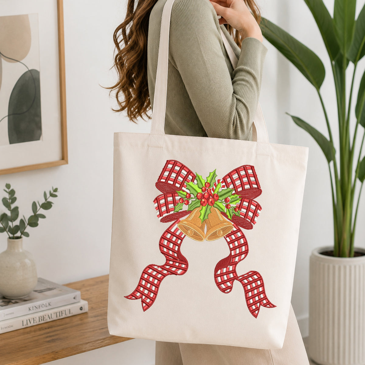 Canvas tote bag decorated with an embroidery design of a red plaid bow with golden holiday bells and holly berries.