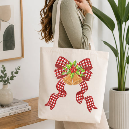Canvas tote bag decorated with an embroidery design of a red plaid bow with golden holiday bells and holly berries.