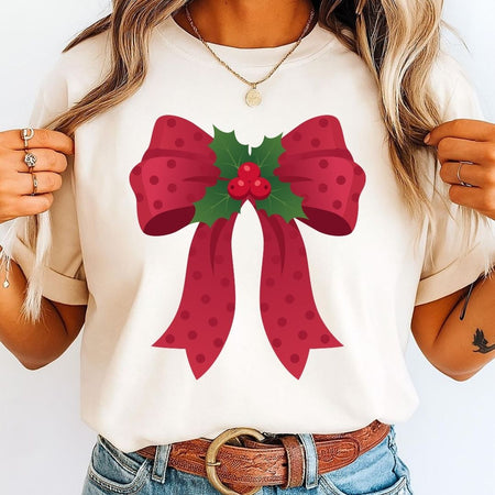 A woman wearing a cream-colored t-shirt with a large red bow and green holly graphic on the front, paired with blue jeans and a brown belt.