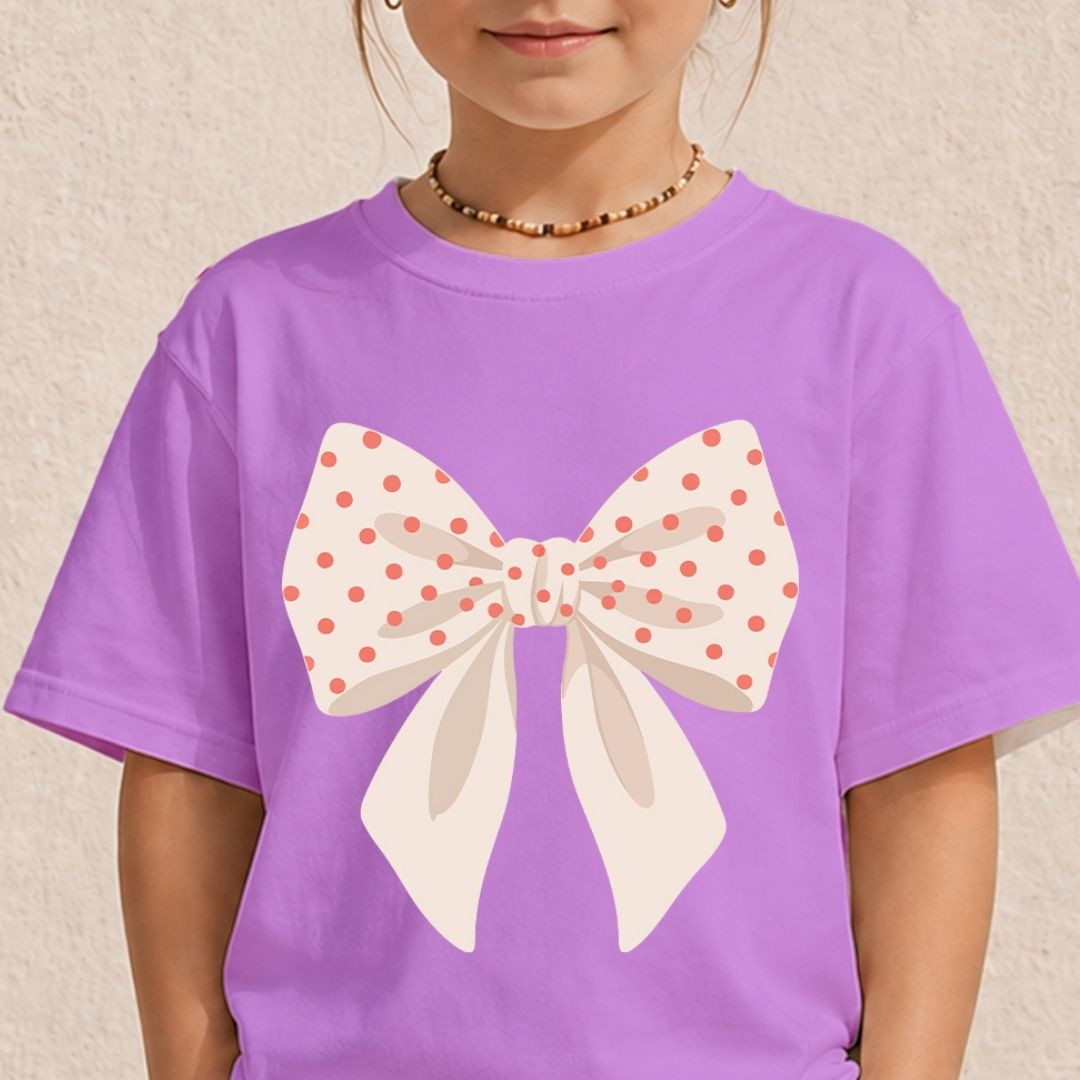 A child wearing a pastel purple t-shirt featuring a large cream bow printed with pink polka dots.