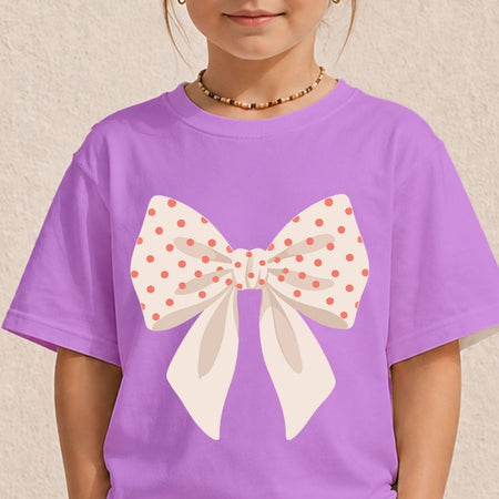 A child wearing a pastel purple t-shirt featuring a large cream bow printed with pink polka dots.