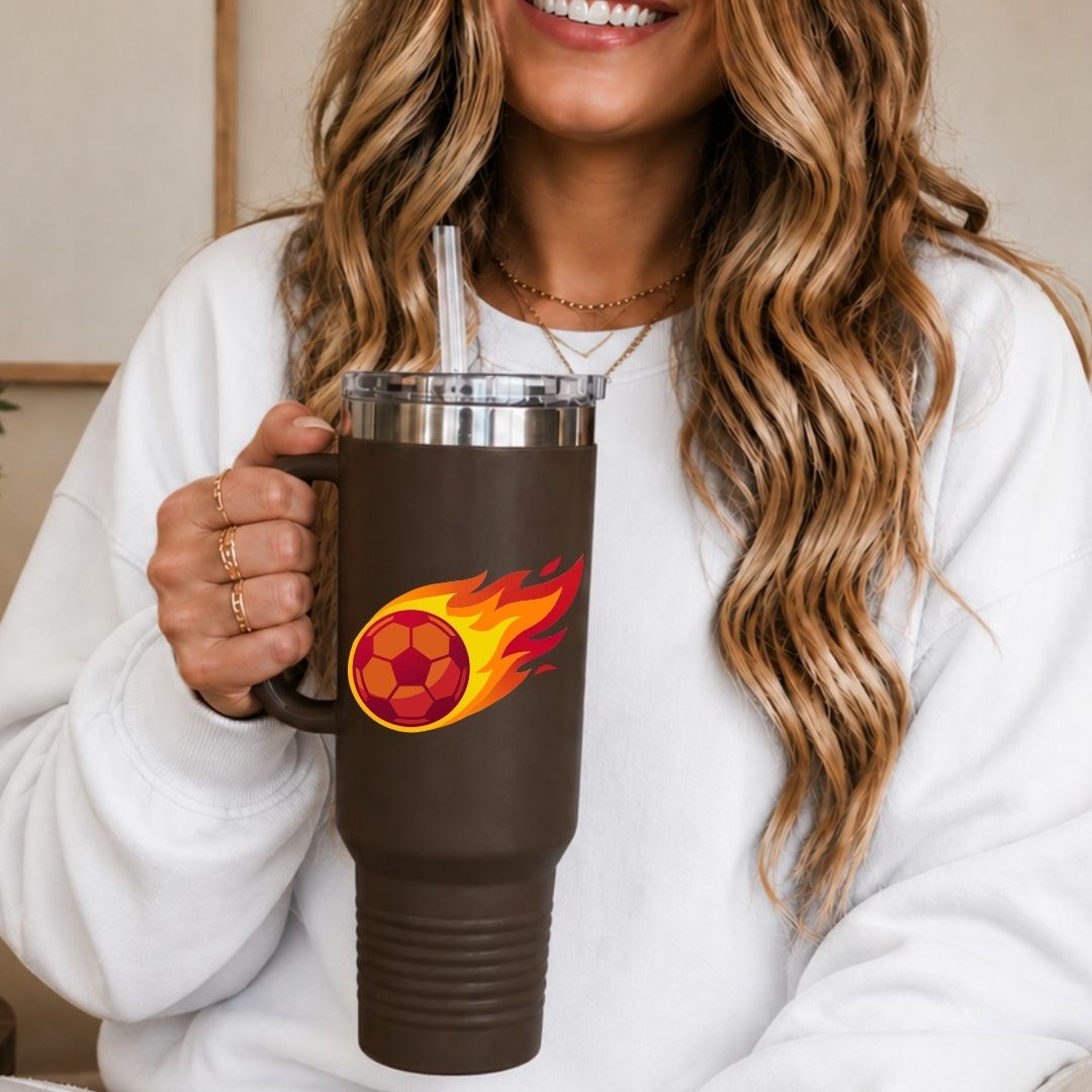 A woman holding a dark brown 40oz travel tumbler with a handle, custom printed with a bold red soccer ball wrapped in vibrant orange and red speed flames.