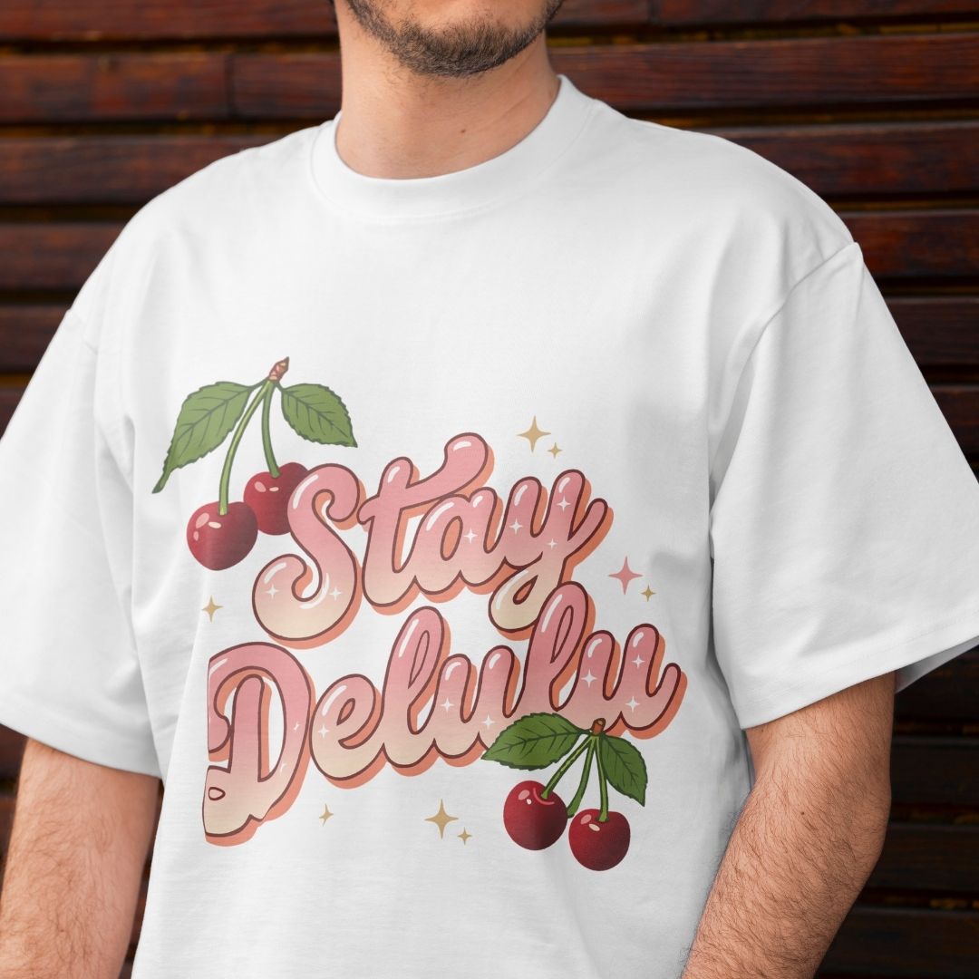White t-shirt with 'Stay Delulu' graphic and cherries on a wooden background