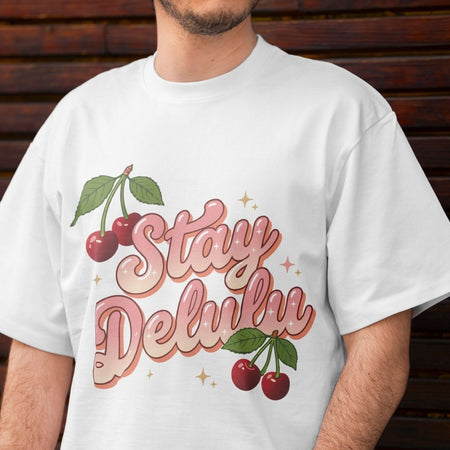 White t-shirt with 'Stay Delulu' graphic and cherries on a wooden background