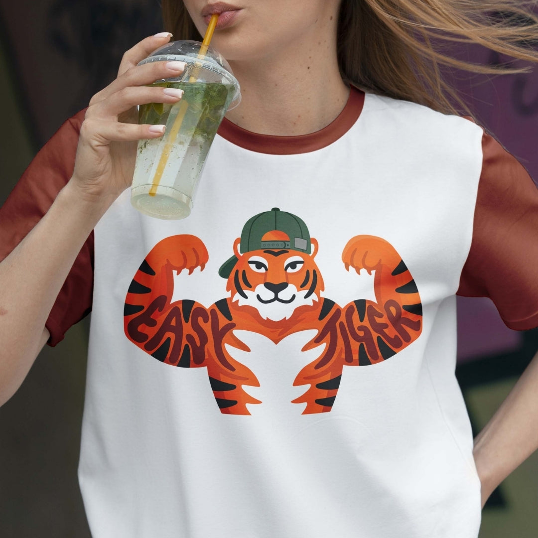 Person wearing a white t-shirt with a tiger graphic and 'EAST TIGER' text, holding a drink.