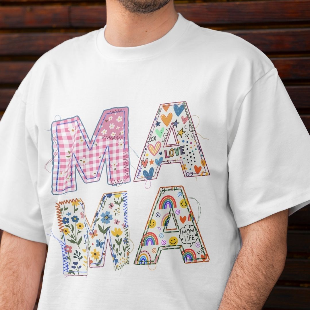 White t-shirt with colorful 'MAMA' text design on a wooden background