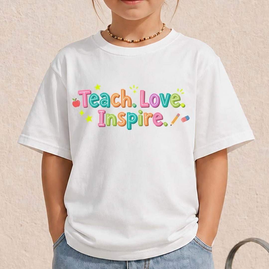 White t-shirt with colorful 'Teach Love Inspire' text worn by a person on a beige background
