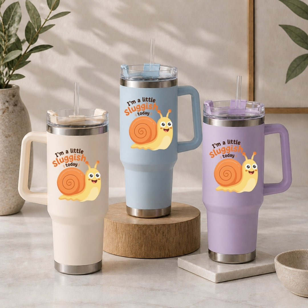 Three stainless steel tumblers in cream, light blue, and light purple, each decorated with the same cute, smiling cartoon snail graphic and the text "I’m a little sluggish today."