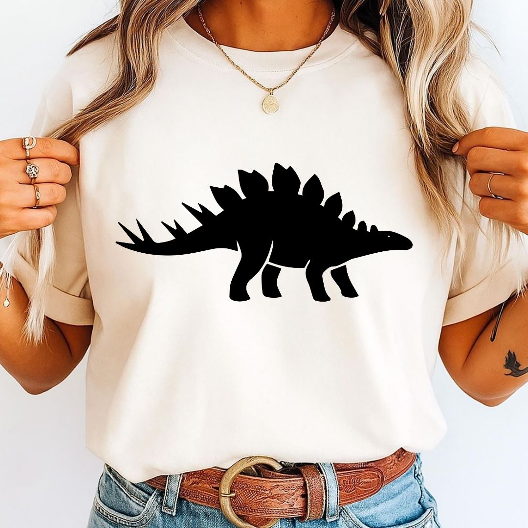 A woman wearing a cream-colored short-sleeve t-shirt with a black Stegosaurus dinosaur silhouette printed on the front, paired with blue jeans and a brown leather belt.