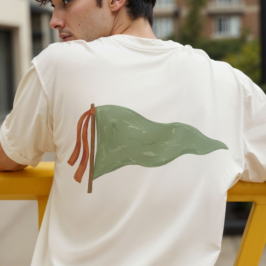 Person wearing a white t-shirt with a green leaf design on the back, sitting outdoors.