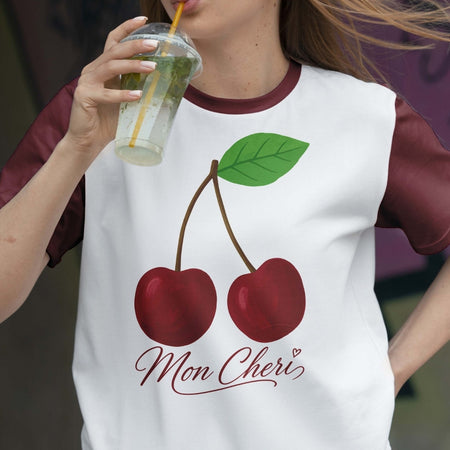 Person wearing a white t-shirt with cherry design and 'Mon Cheri' text, holding a drink.