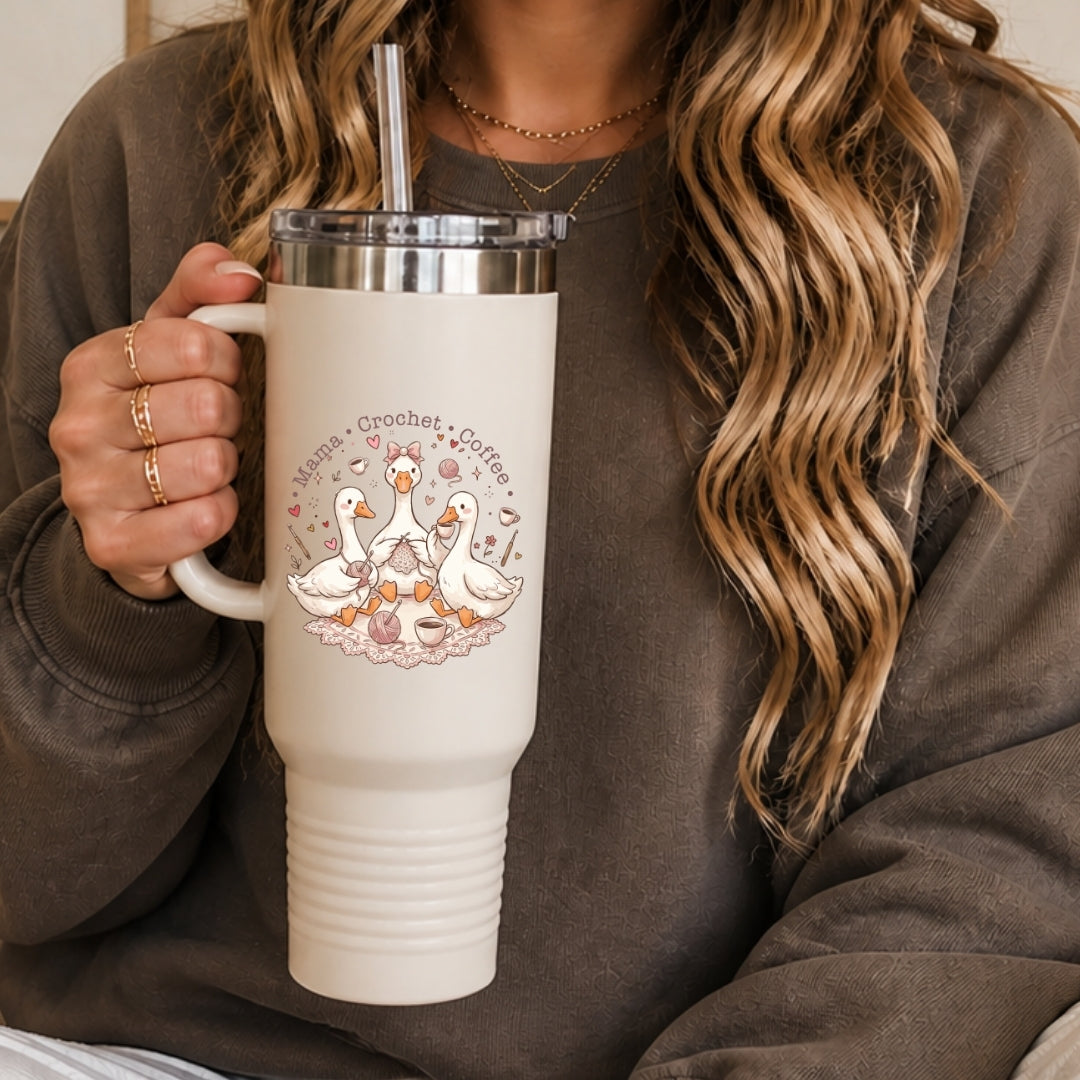 Close-up of a person in a brown sweatshirt holding a large white insulated travel tumbler with a handle, customized with a whimsical "Mama Crochet Coffee" illustration.