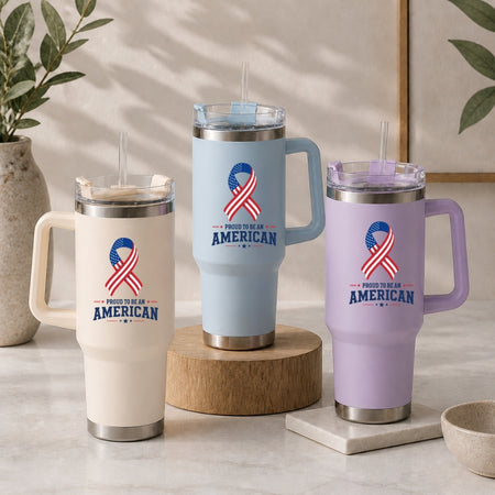 Three stainless steel tumblers in cream, light blue, and light purple, each decorated with an American flag ribbon graphic and the text "Proud to be an American."