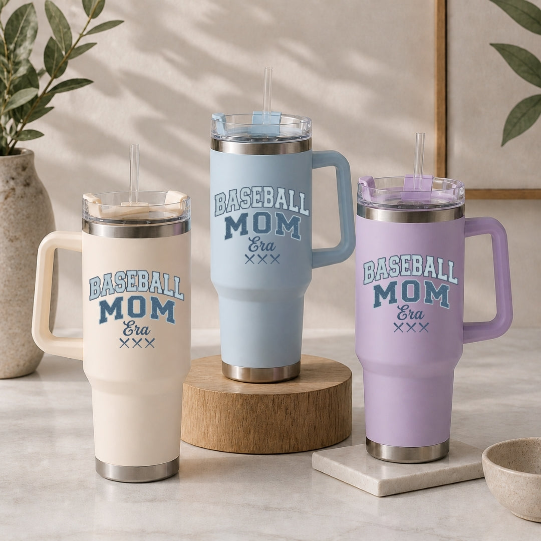 Three insulated travel tumblers with handles and straws in cream, light blue, and pastel purple, all customized with the "Baseball Mom Era" design.