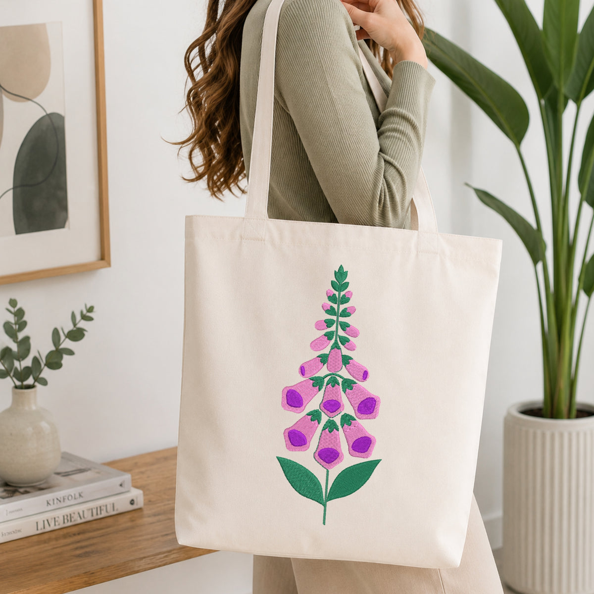 Woman carrying a beige canvas tote bag styled with a purple and green foxglove embroidery pattern.