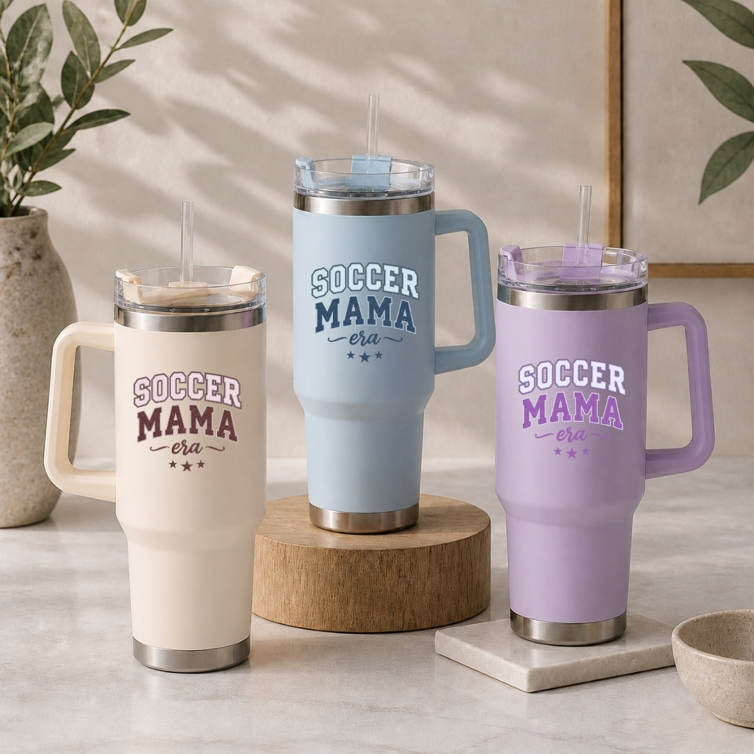 Three insulated travel tumblers with handles and straws in cream, light blue, and pastel purple, all featuring the custom "Soccer Mama Era" design.