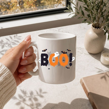White travel tumbler with a black straw featuring a spooky "BOO!" Halloween design, set against a nature background.