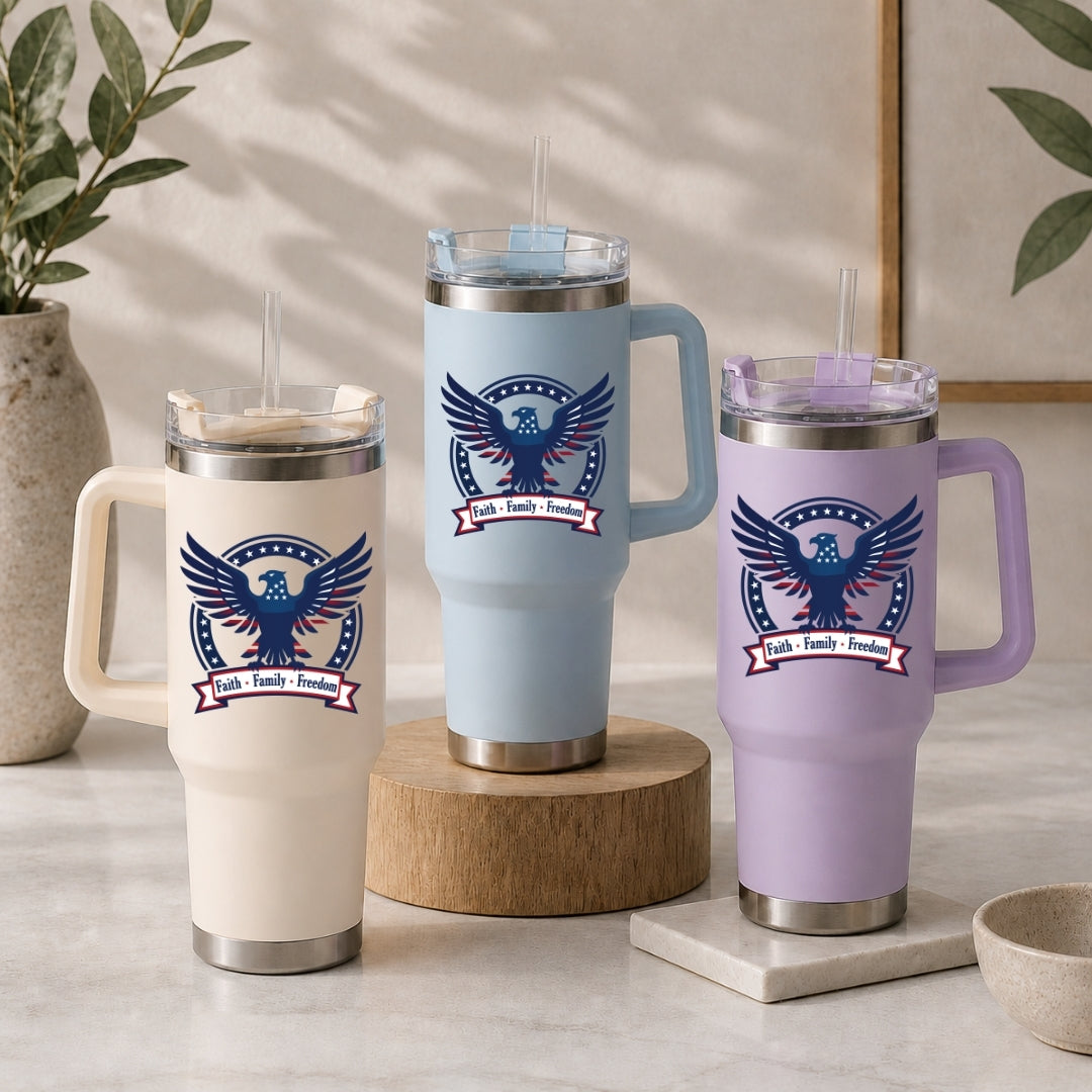 Three stainless steel tumblers in cream, light blue, and light purple, each decorated with the same patriotic eagle graphic and the text "Faith • Family • Freedom".