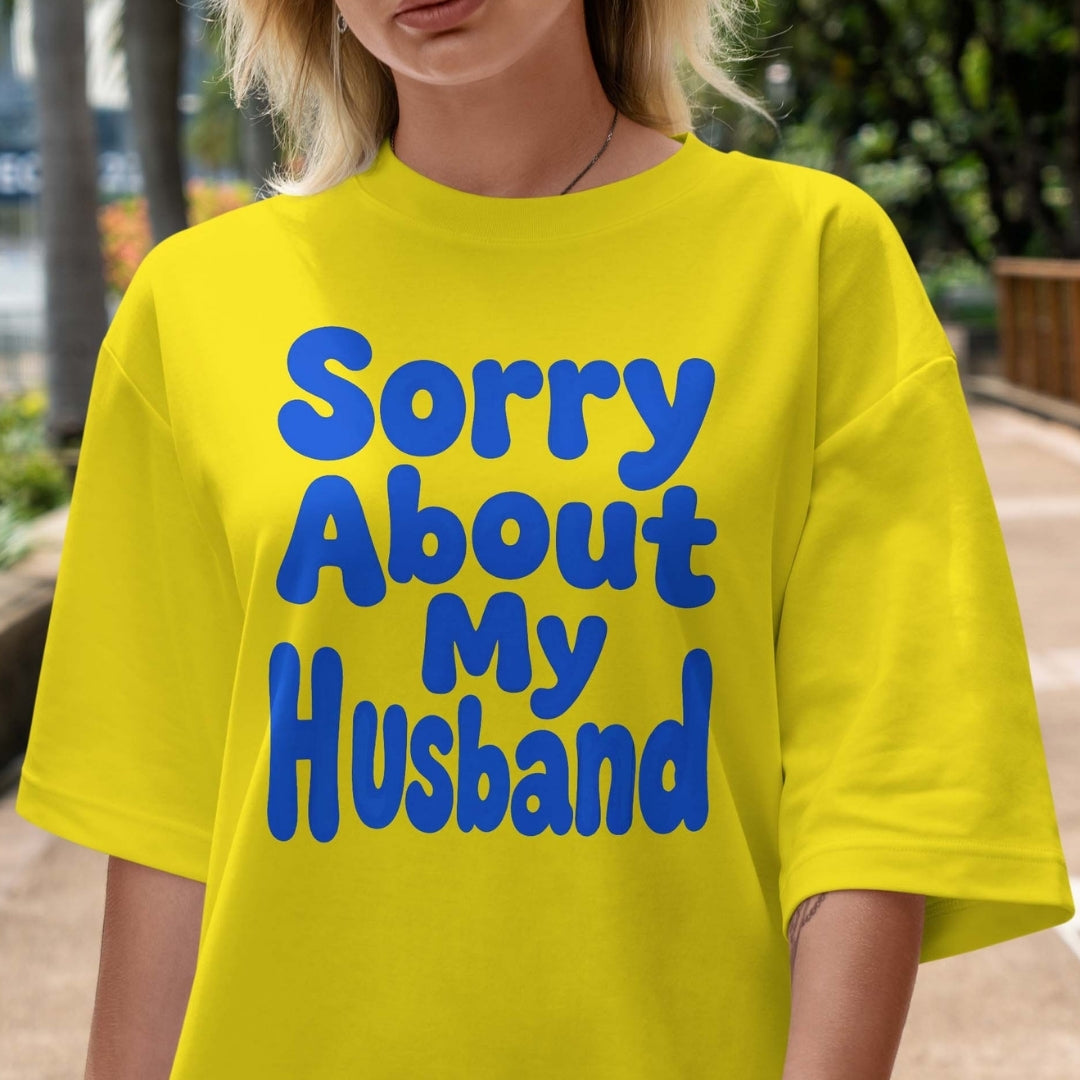 Person wearing a yellow t-shirt with blue text 'Sorry About My Husband' outdoors.