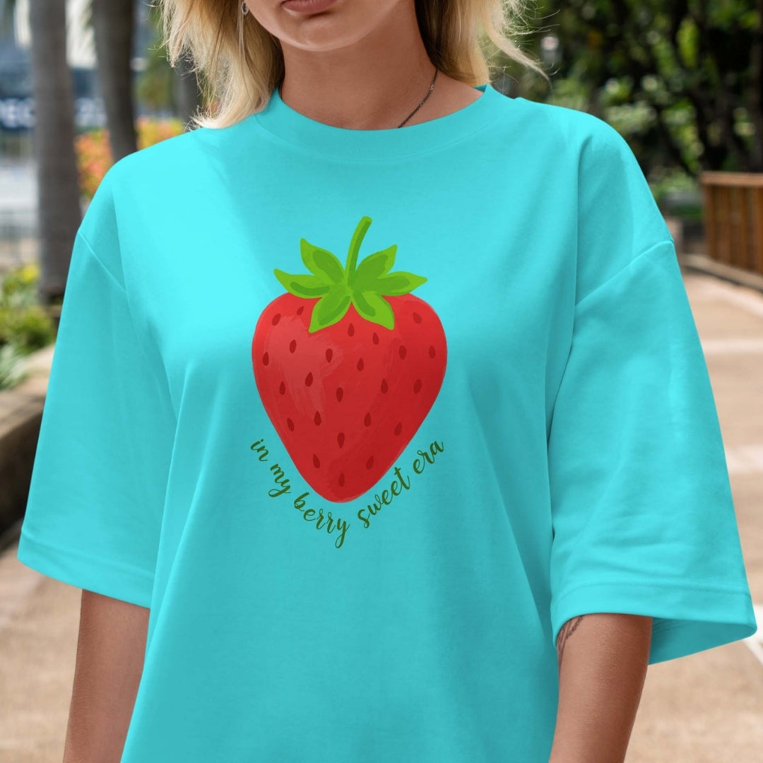 Person wearing a turquoise t-shirt with a strawberry graphic and text.