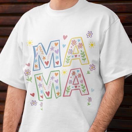 White t-shirt with colorful 'MAMA' text and decorative elements on a wooden background