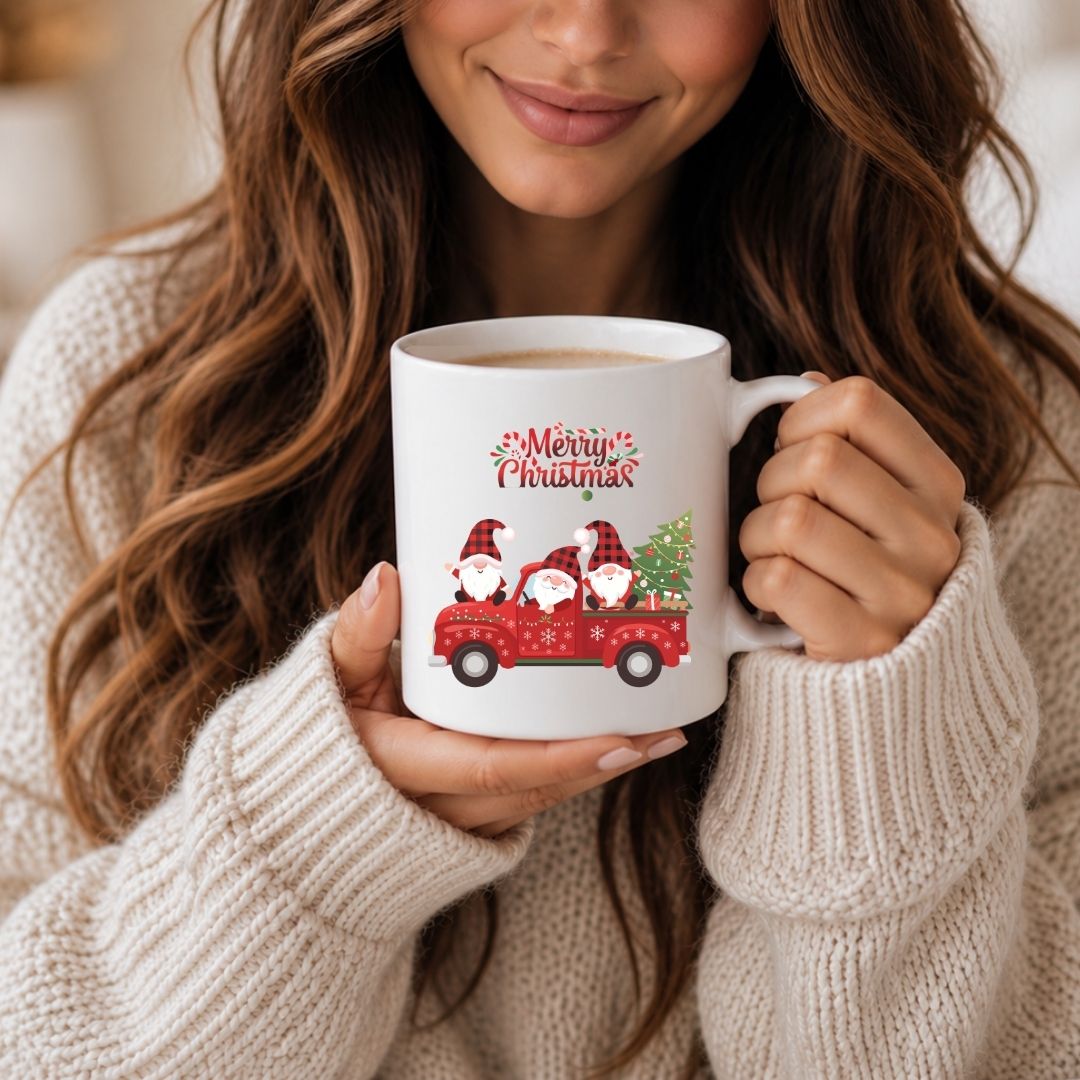 A woman in a cream knit sweater holds a white ceramic mug with a red truck carrying three gnomes and the words 'Merry Christmas' printed on the front.