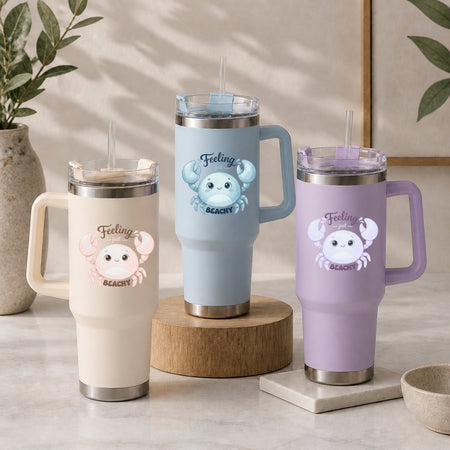 Three stainless steel tumblers in cream, light blue, and light purple, each decorated with a blue cartoon crab graphic and the text "Feeling just BEACHY".