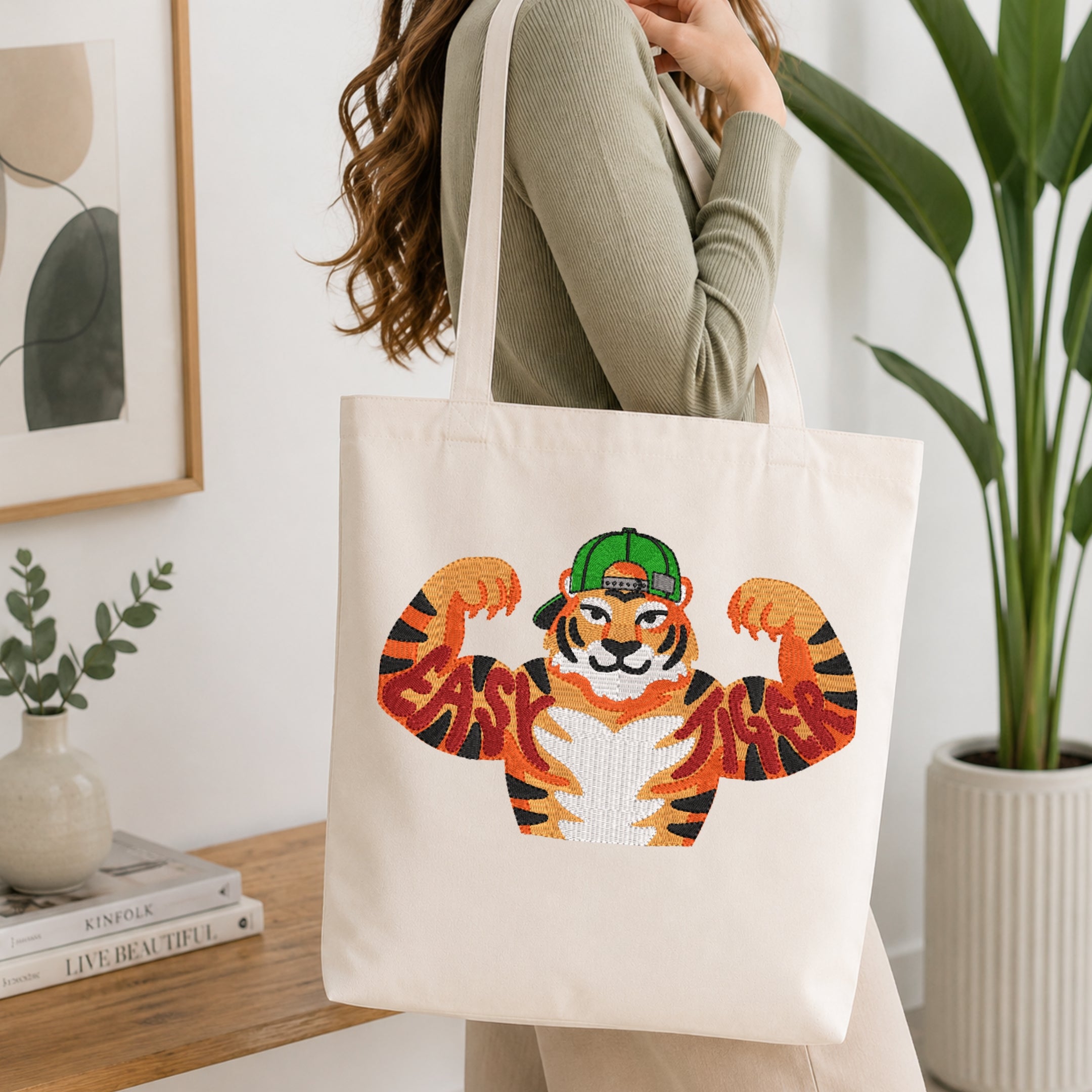 Person holding a canvas tote bag styled with a muscular tiger embroidery design wearing a cap and the text Easy Tiger.