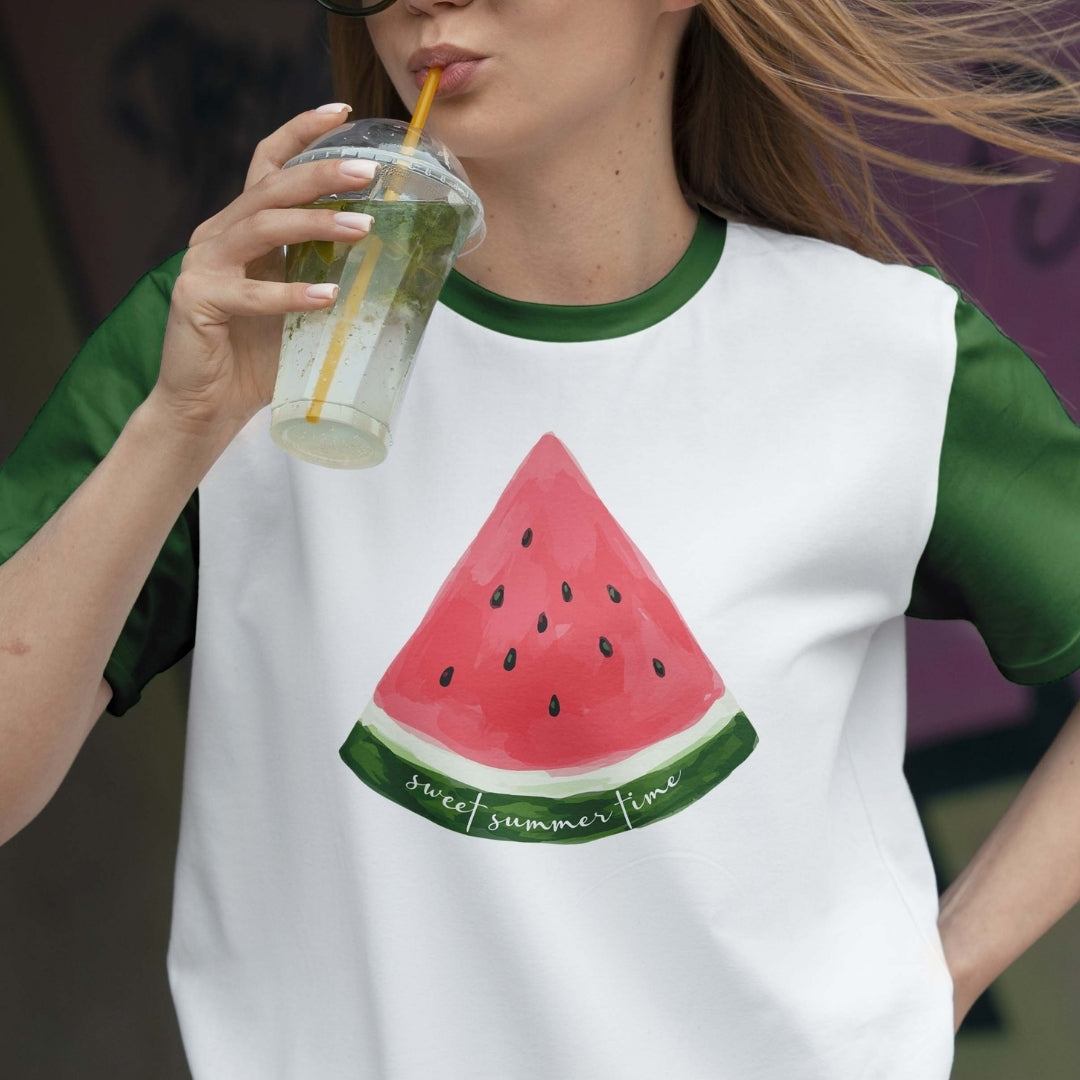 Person wearing a t-shirt with a watermelon design and holding a drink.