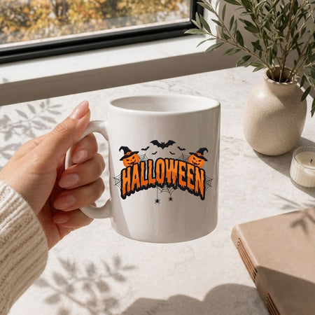Hand holding a white coffee mug printed with a festive "Halloween" pumpkin and bat design, resting on a marble surface.