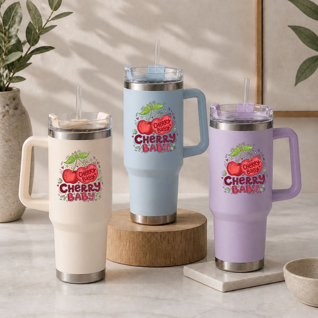 Three insulated handled tumblers with clear lids and straws are displayed on a light stone surface. The tumblers are in cream, light blue, and lavender, each printed with a colorful cherry graphic and the words “Cherry Blast.