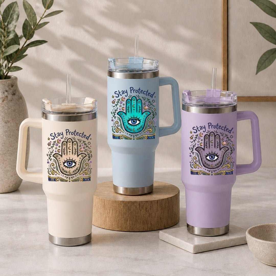 Three insulated tumblers in beige, light blue, and purple, each featuring the spiritual "Stay Protected" Hamsa illustration.