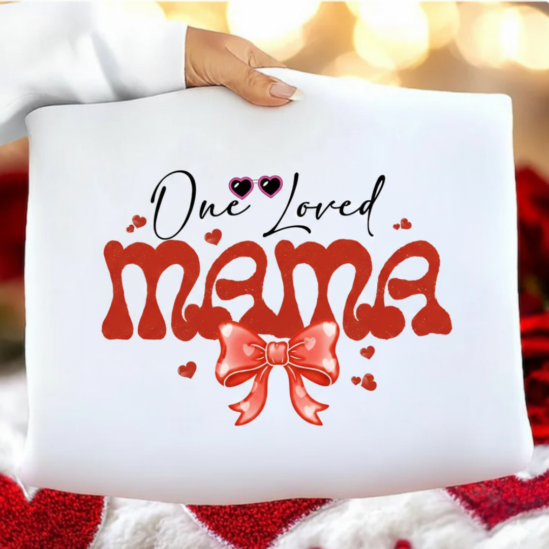 White pillow with 'One Loved Mama' text and a red bow held by a person against a blurred background.