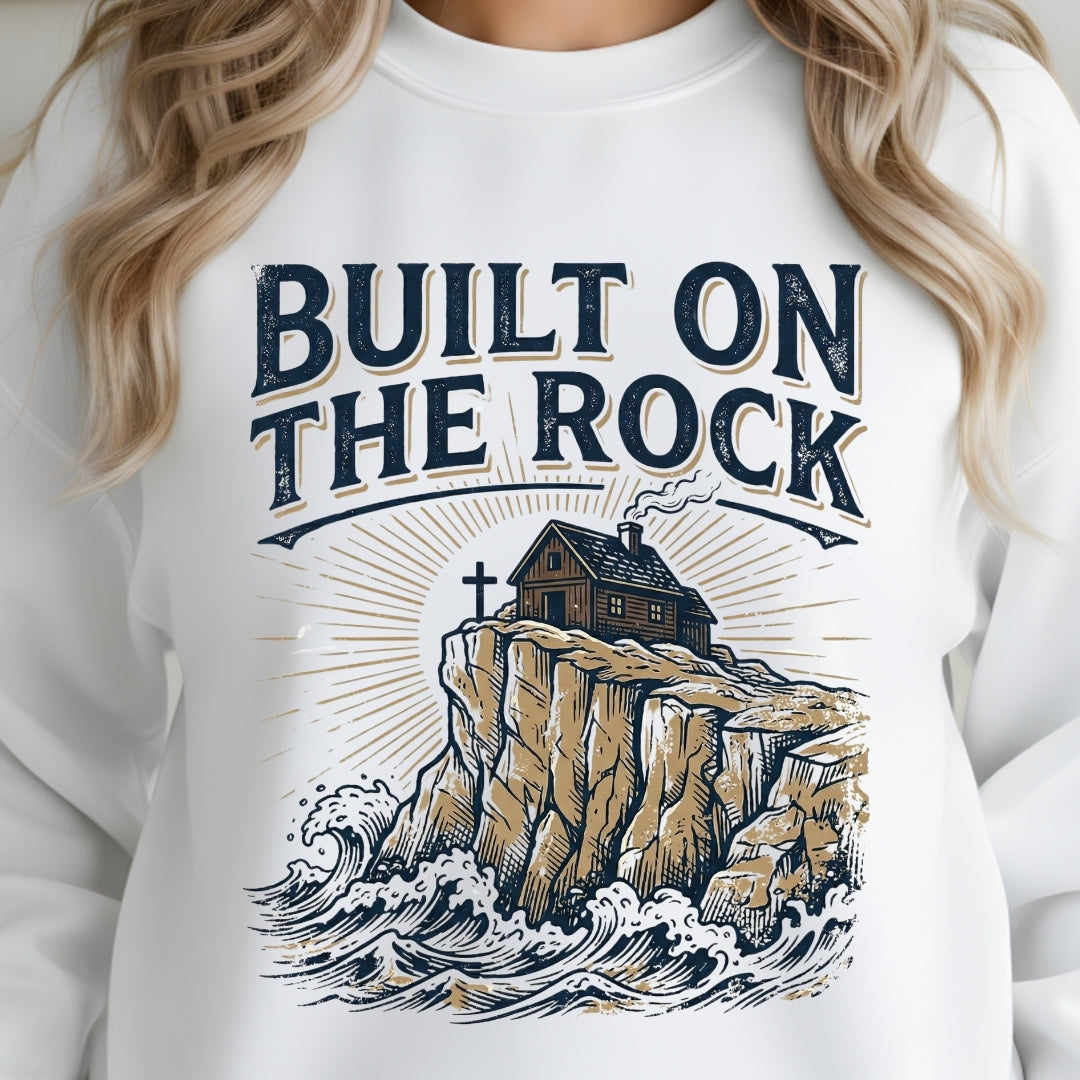 White sweatshirt with 'Built on the Rock' graphic design featuring a house on a cliff.
