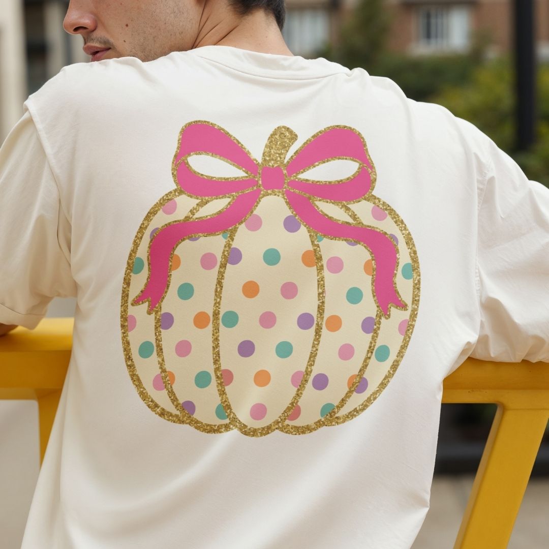 A person wearing a white T-shirt from the back, featuring a large pumpkin graphic with a pink bow, gold glitter outline, and multicolored polka dots.