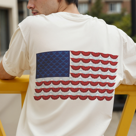 Person wearing a white shirt with an American flag design on the back, sitting outdoors.