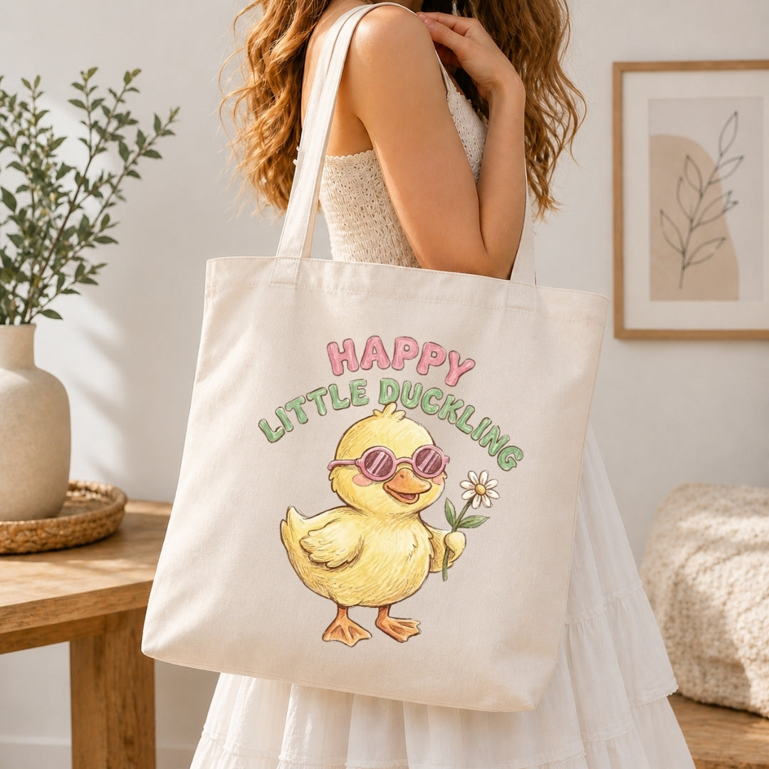 Person holding a tote bag with a duckling design and 'Happy Little Duckling' text.