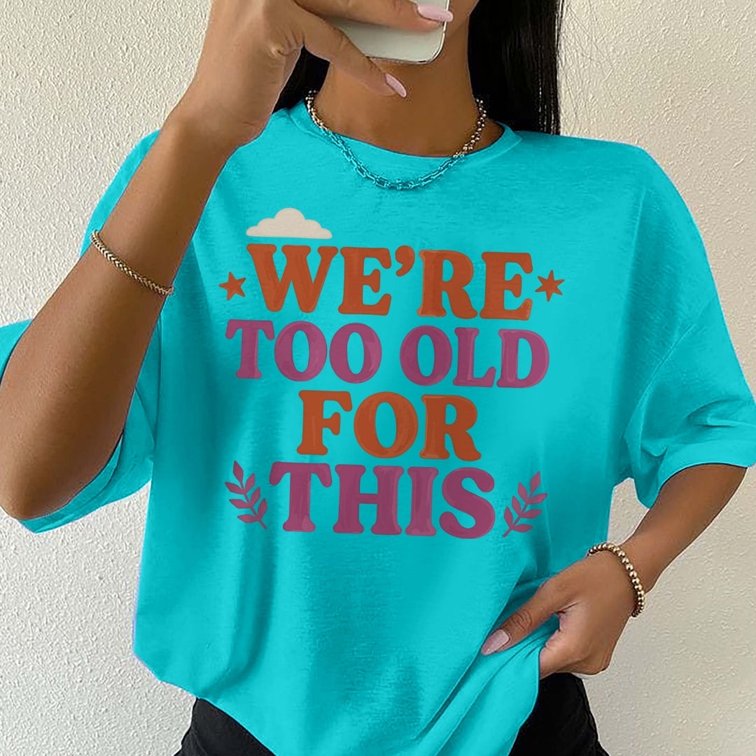 Person wearing a turquoise t-shirt with text 'WE'RE TOO OLD FOR THIS' on a plain background