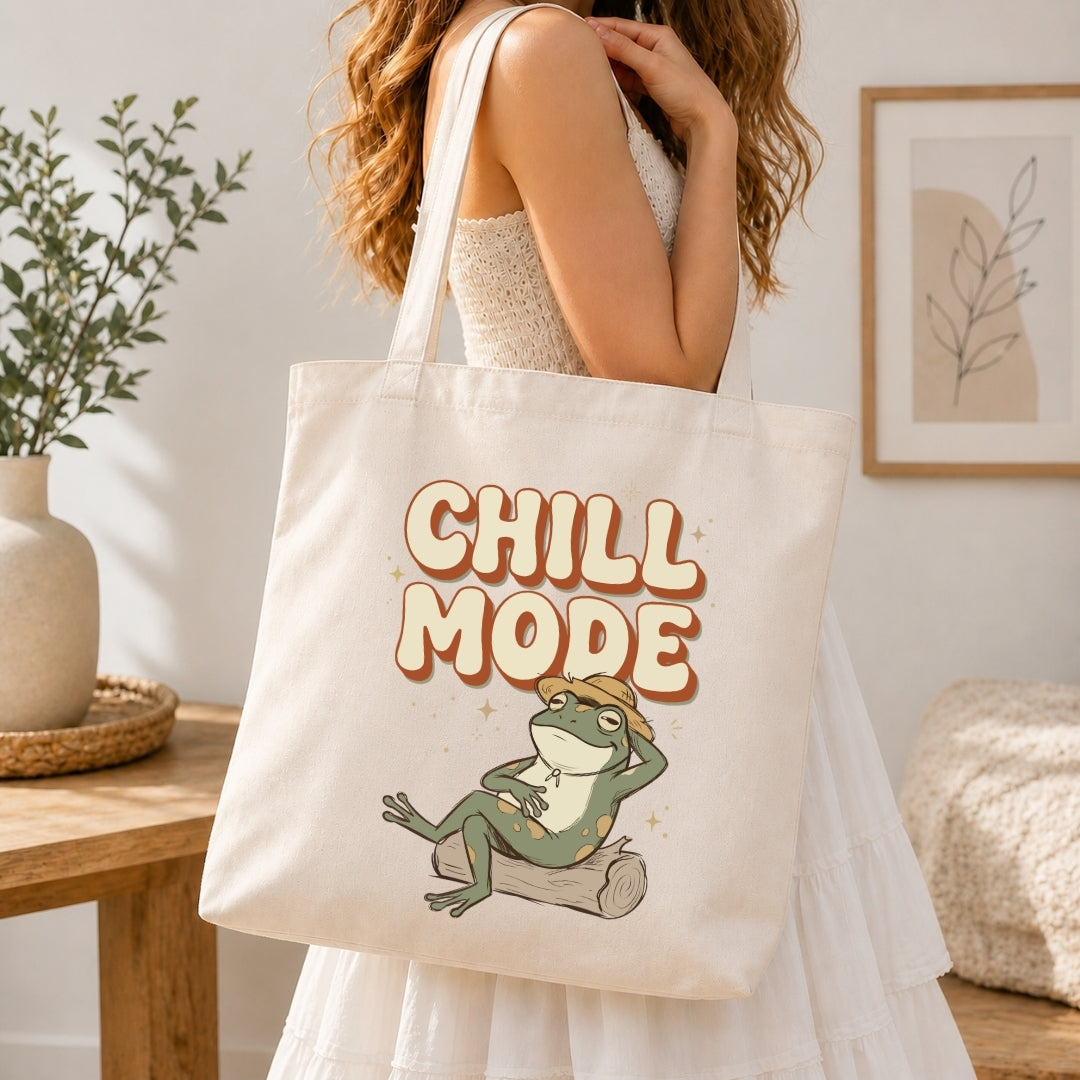 Person holding a tote bag with a frog graphic and 'Chill Mode' text in a home setting.