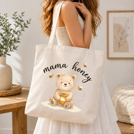 A woman wearing a white dress carries a cream canvas tote bag with a cute cartoon bear holding honey and the words 'mama honey' printed on it, set in a bright, modern room.