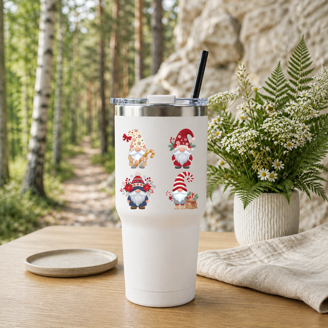 White travel tumbler with a black straw featuring a Christmas gnomes design, placed outdoors near a wooded trail.