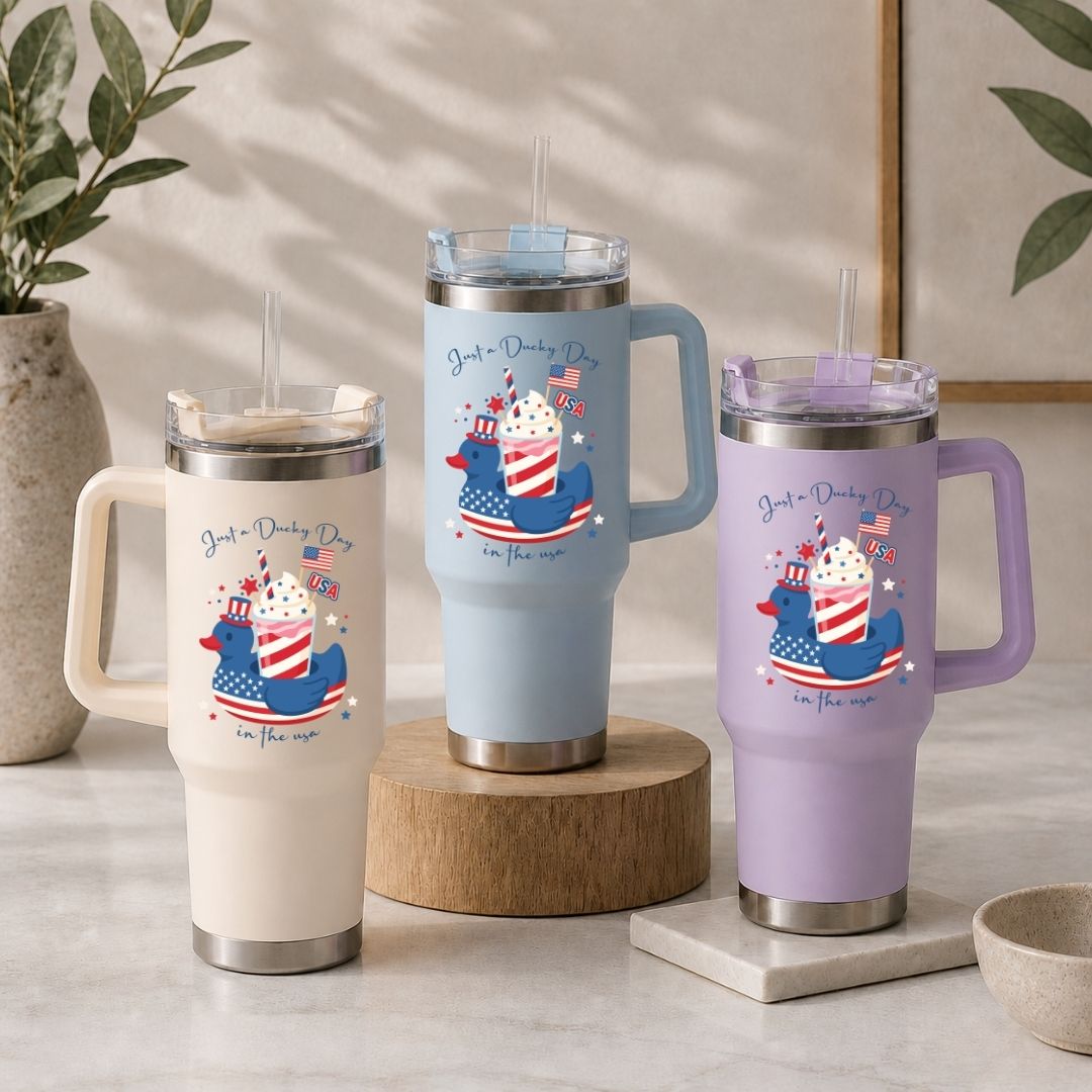 Three insulated travel tumblers in cream, light blue, and lavender purple arranged on a table, all showcasing the "Sippin' on Freedom" design.