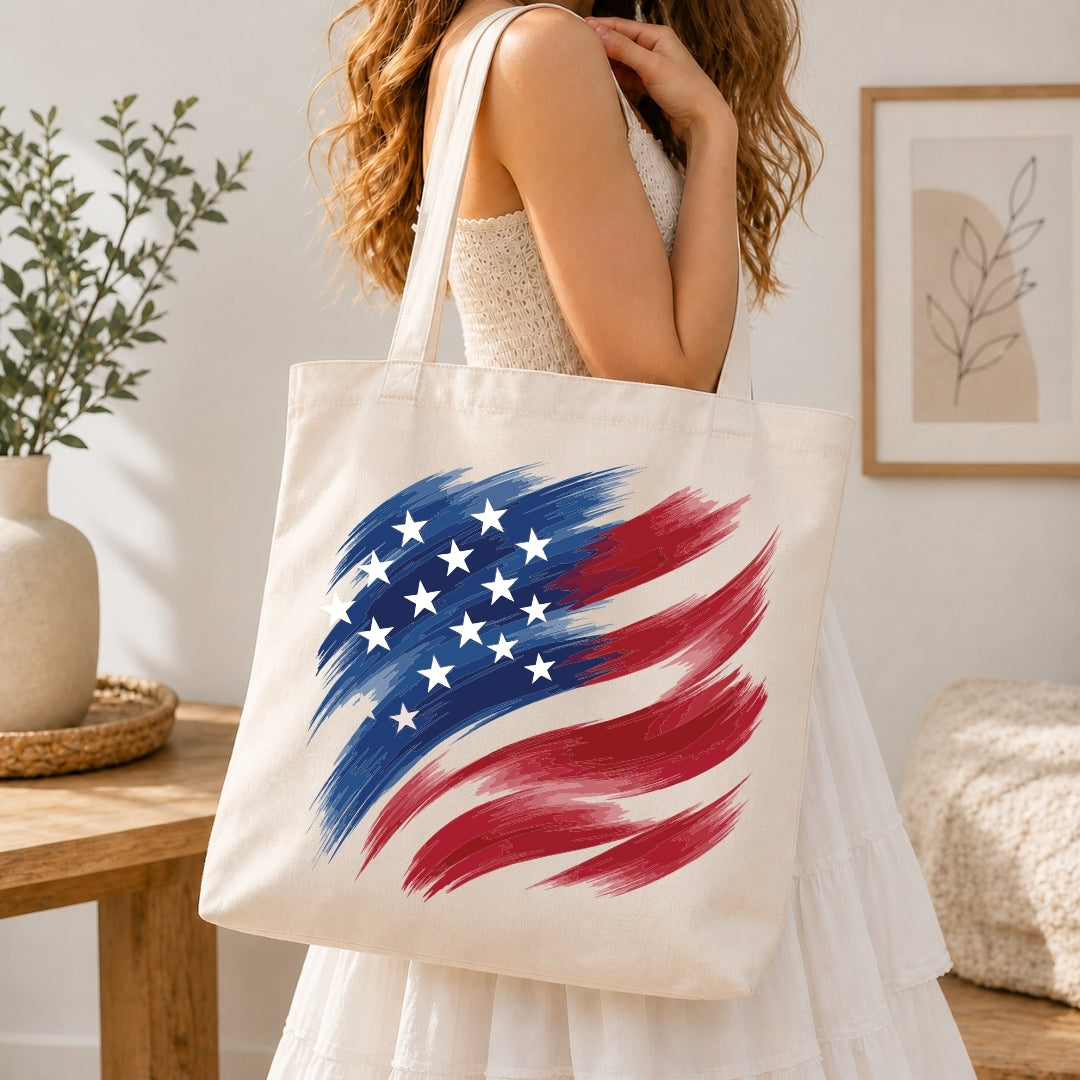 A woman holding a cream-colored tote bag printed with a stylized brushstroke American flag graphic.