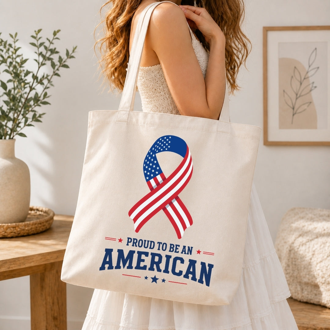 A woman holding a cream-colored tote bag printed with an American flag ribbon graphic and the text "Proud to be an American."