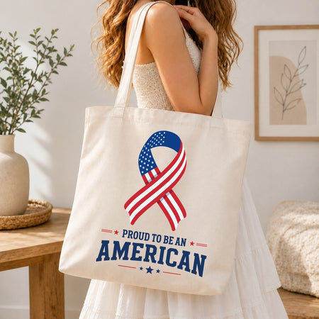 A woman holding a cream-colored tote bag printed with an American flag ribbon graphic and the text "Proud to be an American."
